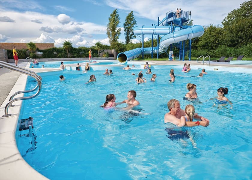 People enjoying a swimming pool with water slide at an accessible holiday park in Lincolnshire