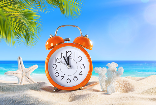 Alarm clock and shells on tropical beach