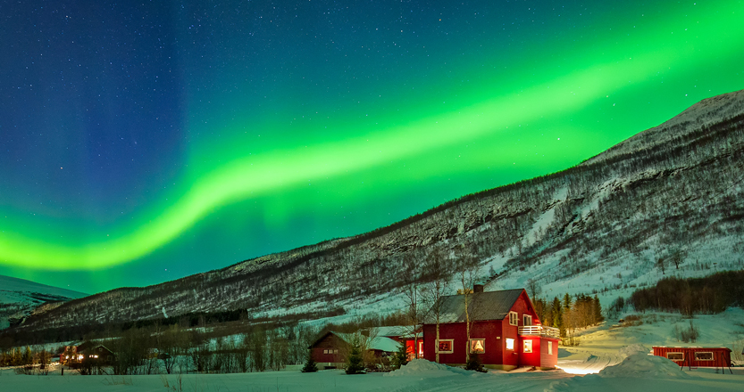 Green Northern Lights over a snowy scene in northern Norway
