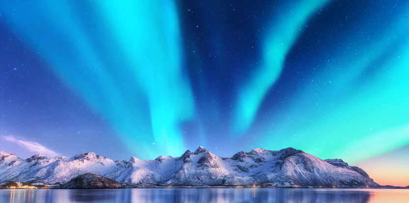 Blue Northern Lights over snowy mountains in Lofoten, Norway