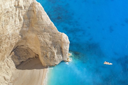 A boat on the sea next to sandy beach and cliffs in the Mediterranean.