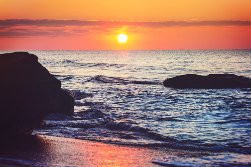 Beautiful sunset on the beach, with sea waves rolling towards the rocks