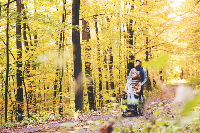 Elderly couple walking through the woods with a wheelchair